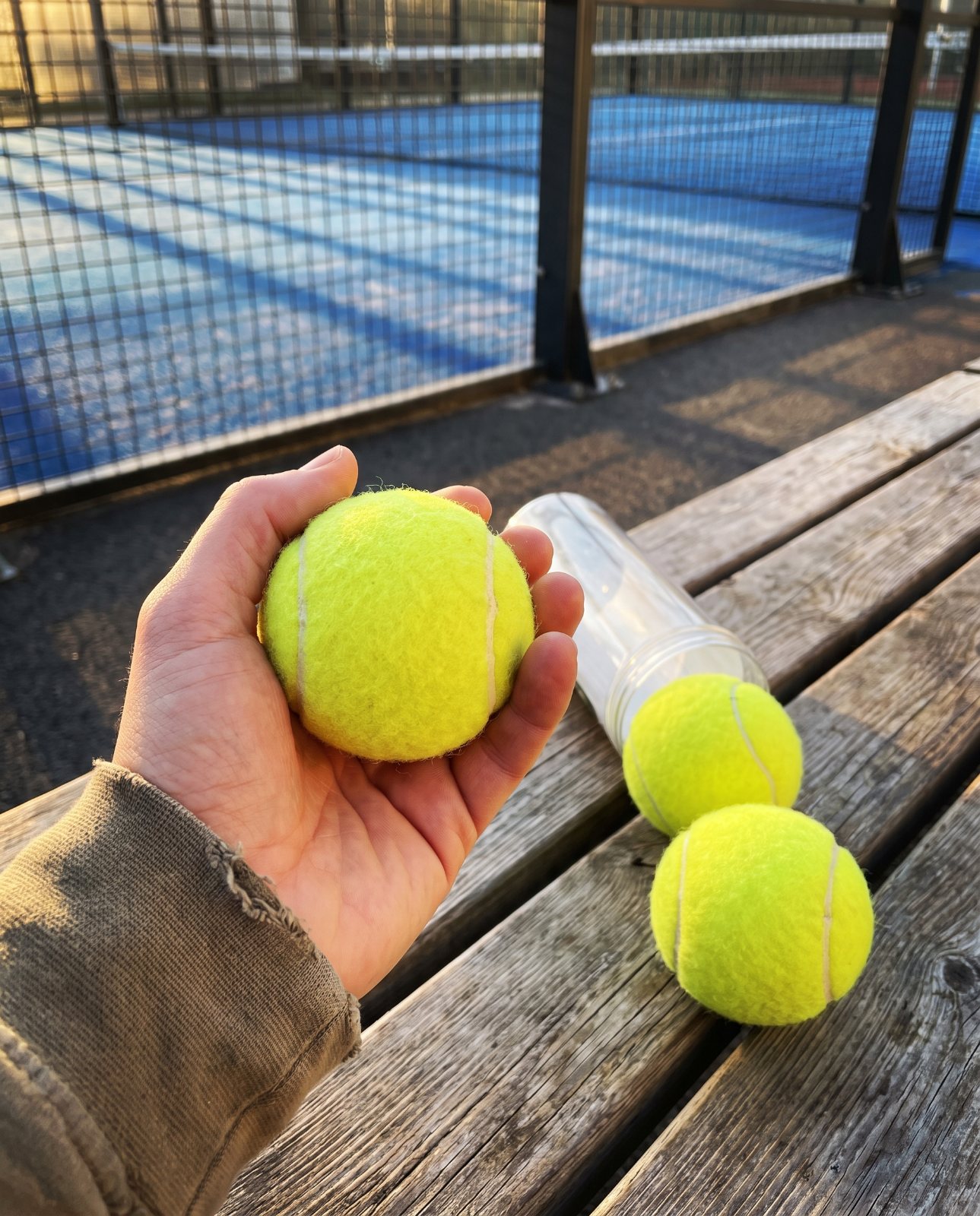 Balles de padel et tube ouvert sur un banc de terrain